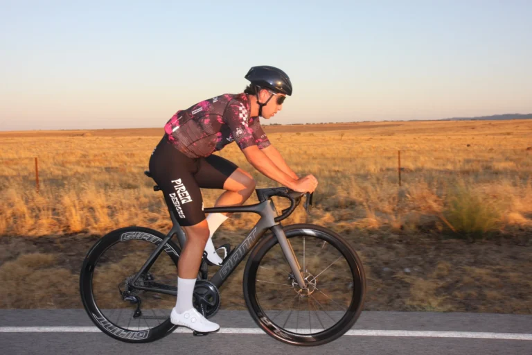 Ciclista con equipación PIREN rodando entre campos al atardecer